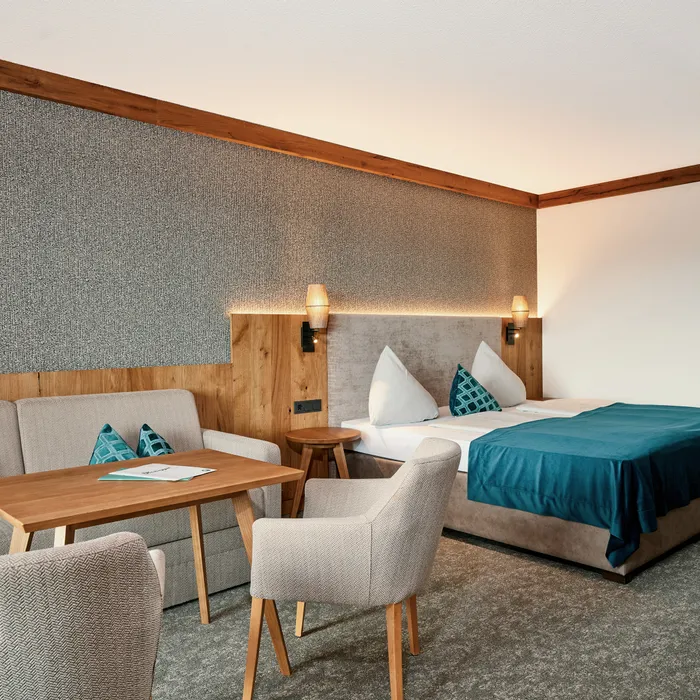 Modernes Hotelzimmer mit Doppelbett, Sofa, Holztisch und türkisfarbenen Akzenten